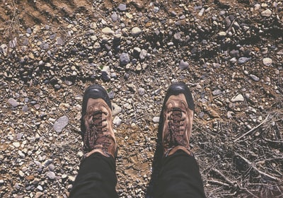 穿着棕色鞋子的人站在泥土和石头地上
